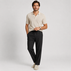 A man modeling a light beige short-sleeve polo shirt and black drawstring trousers against a light gray studio background.