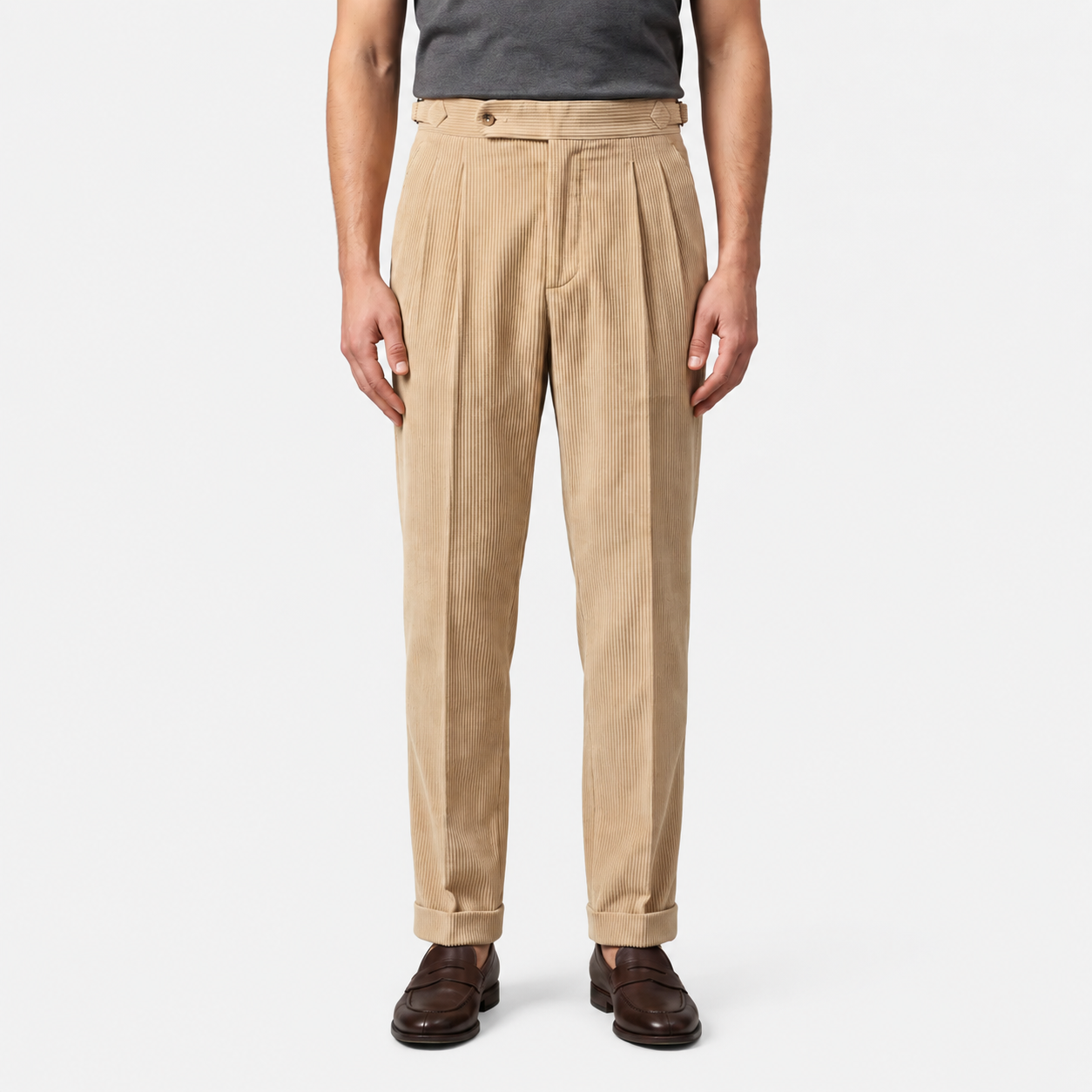 A person wearing beige pleated trousers with a dark gray shirt and brown leather shoes, shown from the waist down against a light gray studio background.