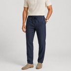 A man wearing dark navy drawstring trousers, a cream polo shirt, and tan loafers, standing against a light gray studio background.