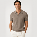A man wearing a short-sleeve knit polo shirt in taupe brown with white trousers, standing against a light gray studio background.
