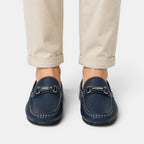 Navy loafers with metallic accents worn with beige pants on a white background