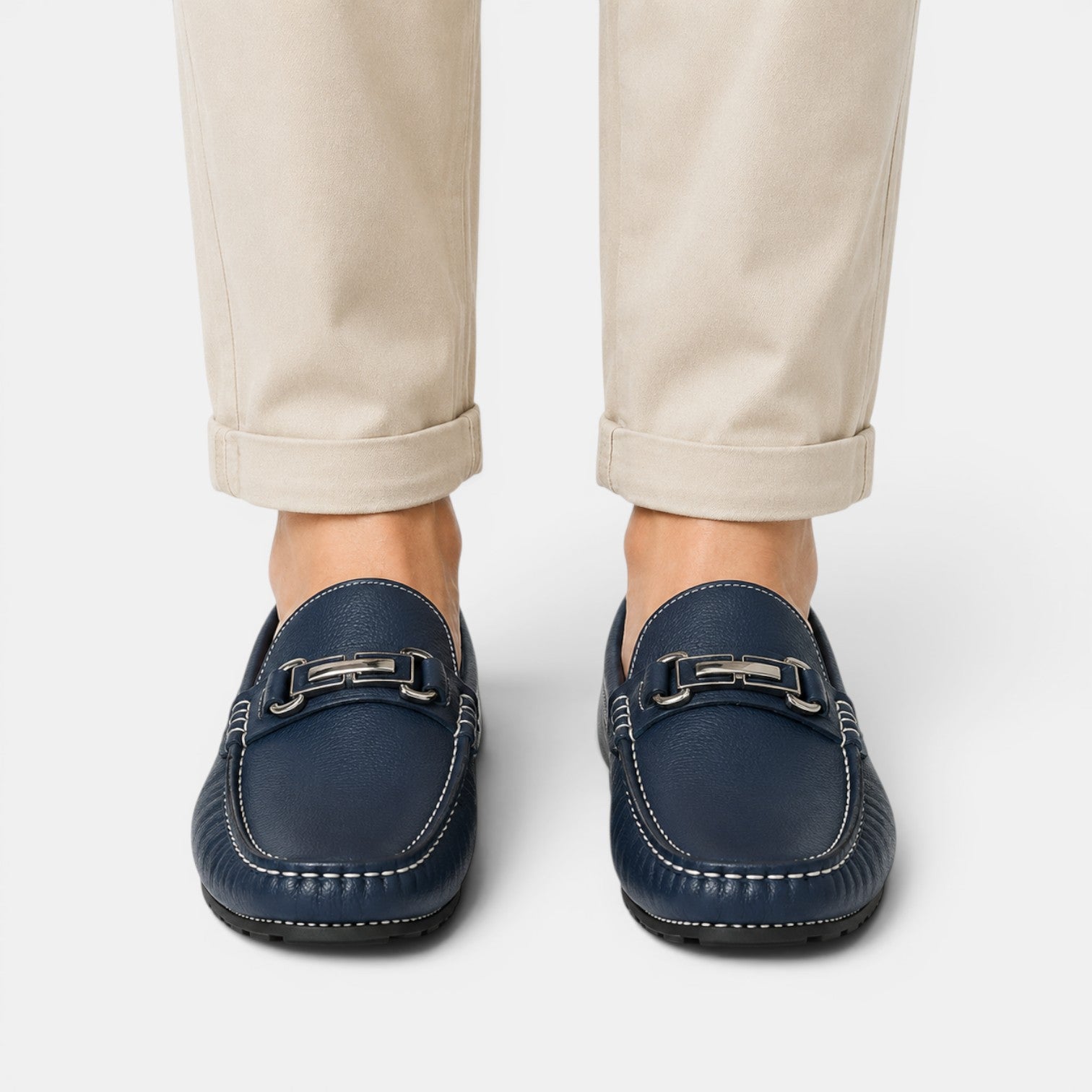 Navy loafers with metallic accents worn with beige pants on a white background