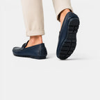 Navy loafers worn with beige pants on a white background