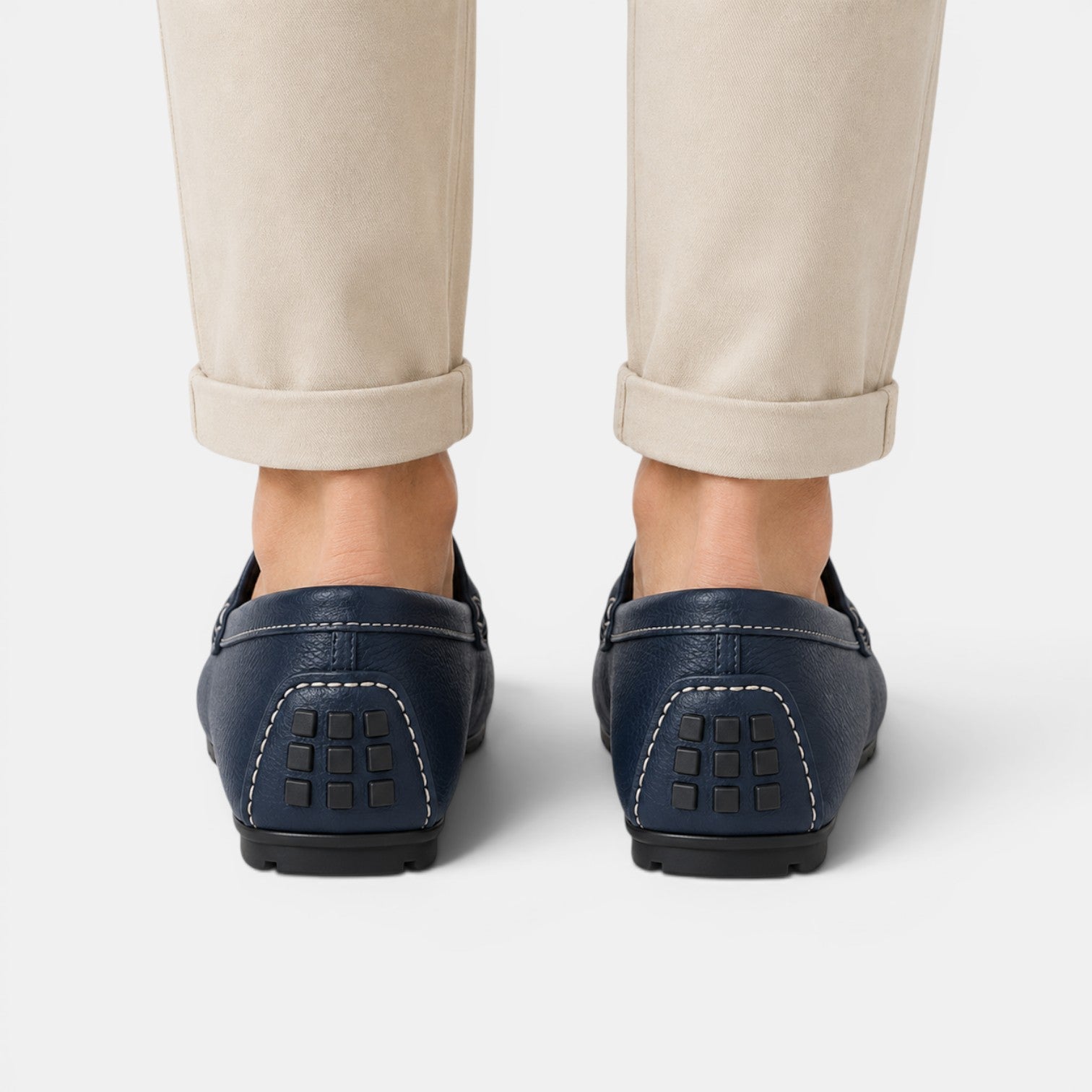 Navy loafers worn with beige pants on a white background