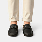 Black loafers worn with beige pants on a light gray background