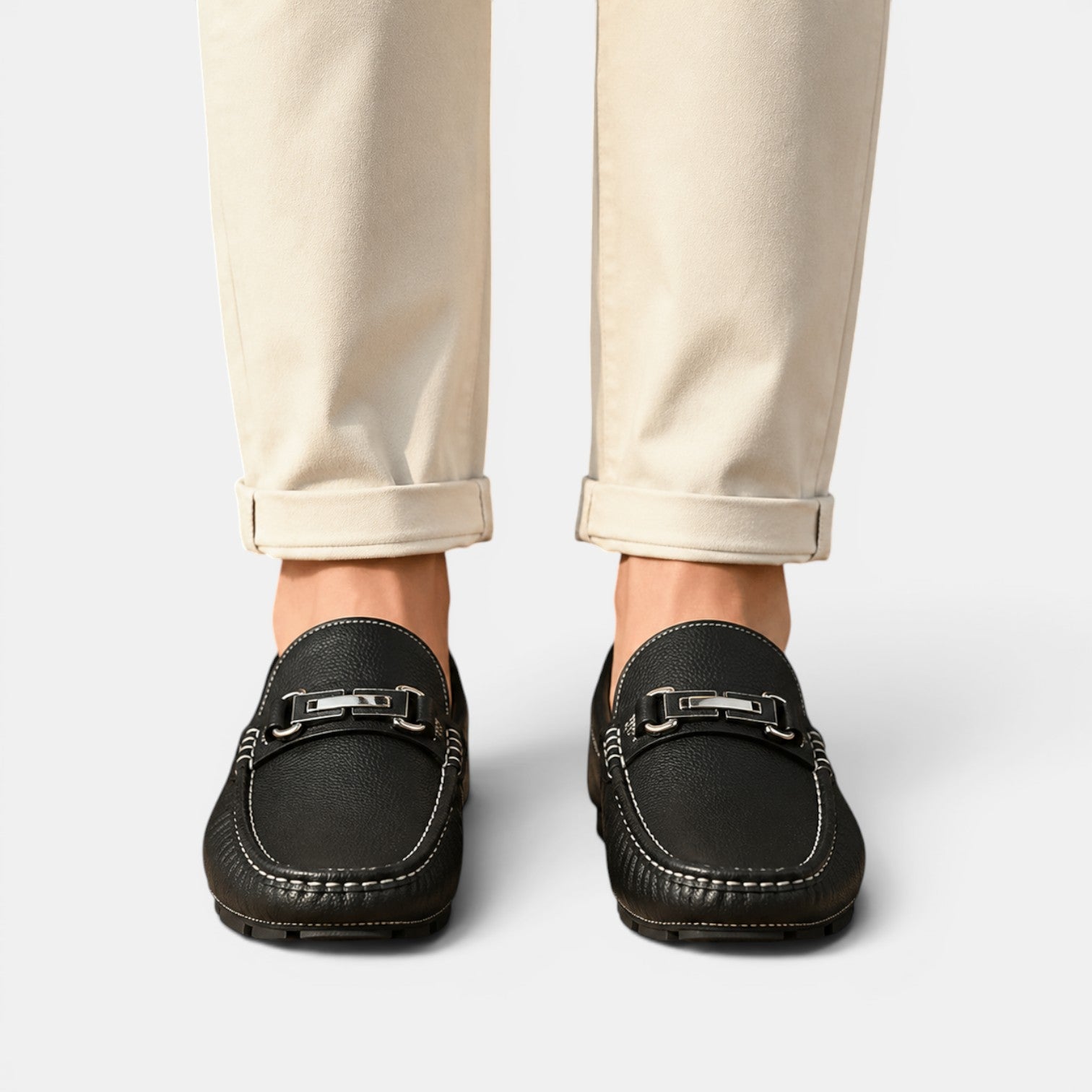 Black loafers worn with beige pants on a light gray background