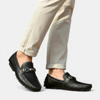 Black loafers worn with beige pants on a light gray background