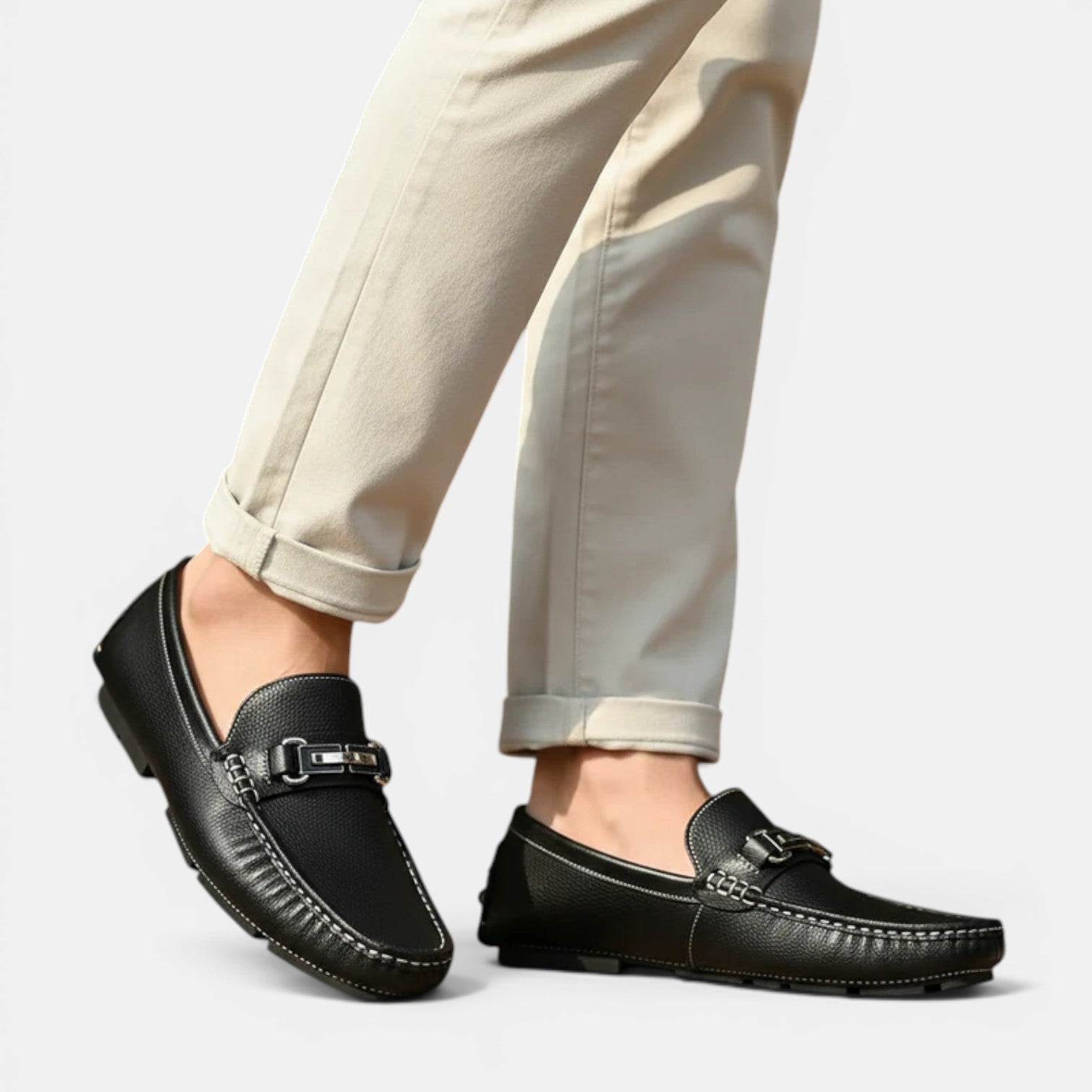 Black loafers worn with beige pants on a light gray background