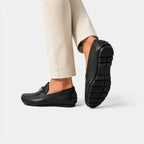Black loafers worn with beige pants on a white background