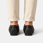 Black loafers worn with beige pants on a light gray background