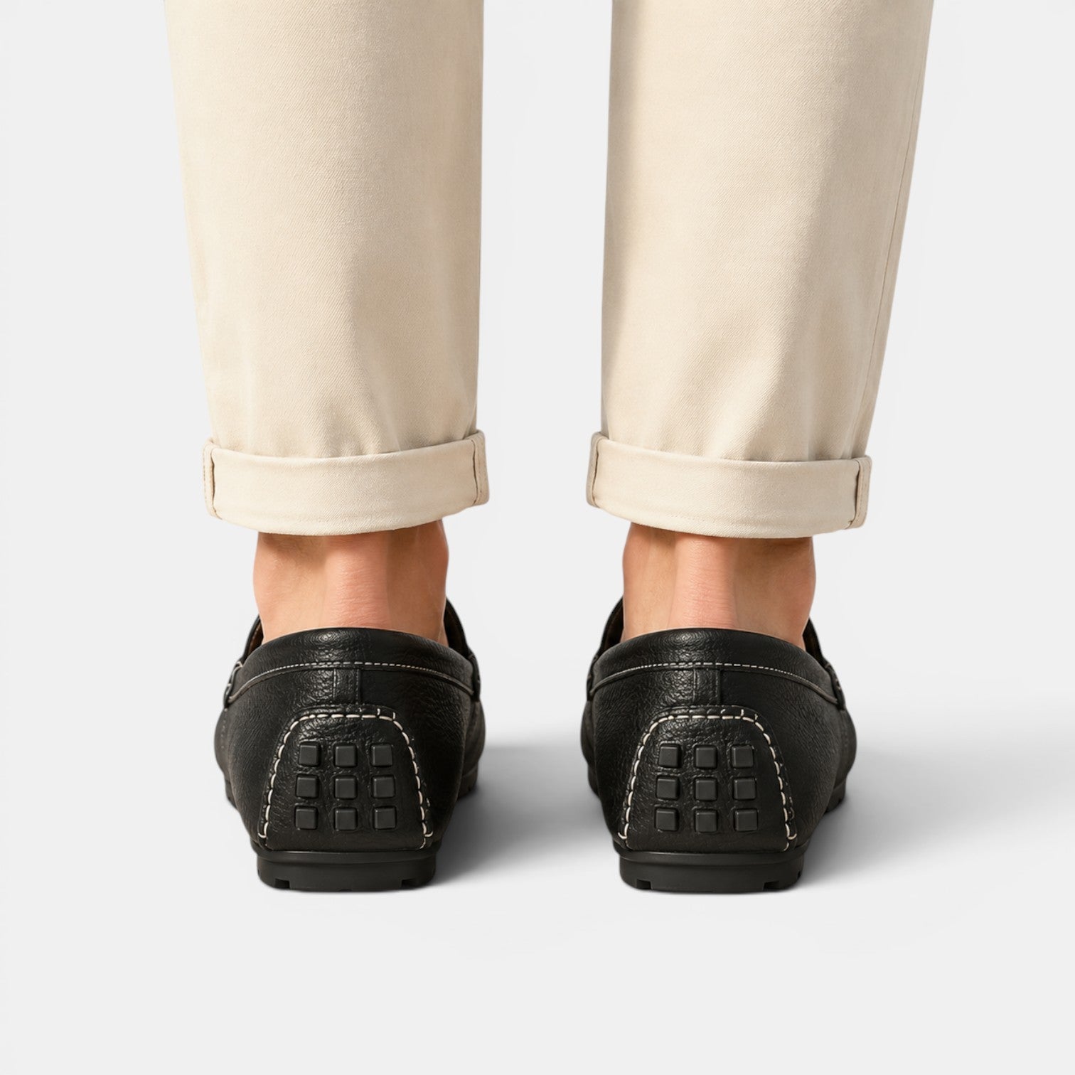 Black loafers worn with beige pants on a light gray background