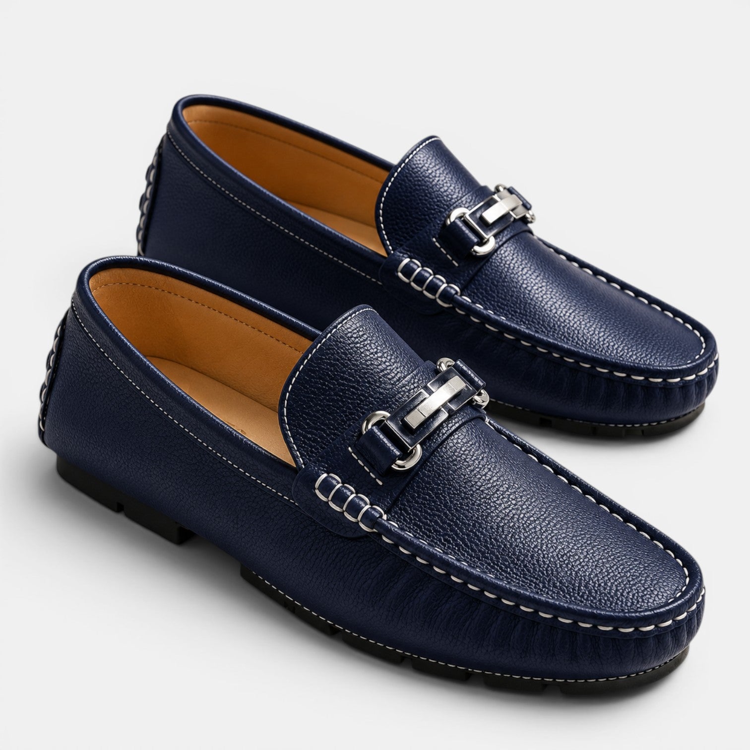 Pair of navy blue loafers with silver buckles on a light gray background