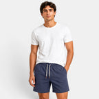 Man wearing a white t-shirt and navy shorts on a plain background