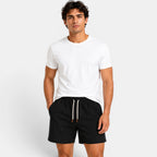 Man wearing a white t-shirt and black shorts on a light gray background