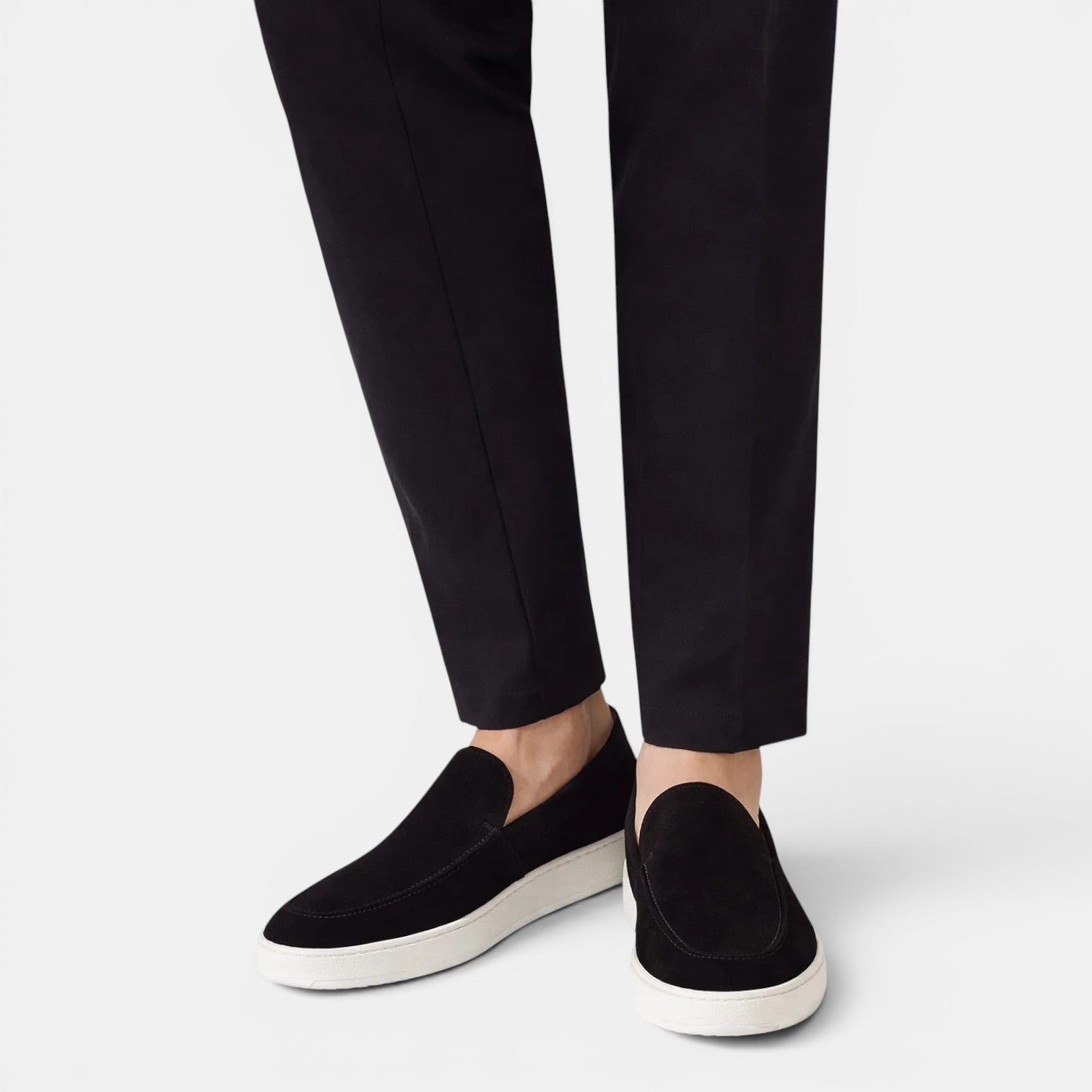 Black loafers worn with black pants on a light gray background