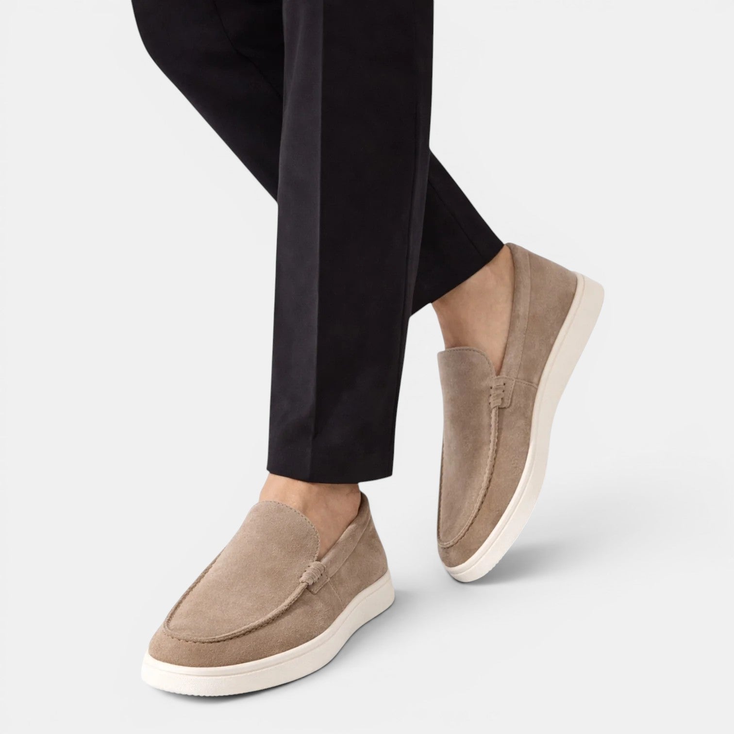 Beige loafers worn with black pants on a light gray background