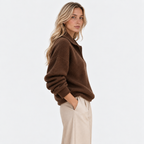 Side view of a woman wearing a brown knit pullover sweater with cream trousers