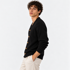 Side view of a man wearing a black ribbed knit cardigan with white trousers