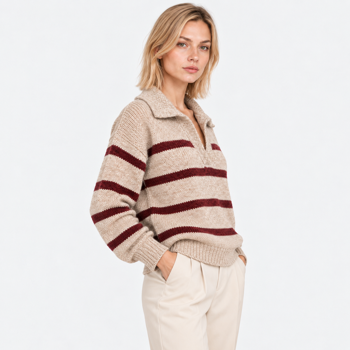 Side view of a woman wearing a beige and burgundy striped knit sweater with white pants