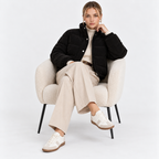 Woman wearing a black quilted puffer jacket with cream trousers while seated