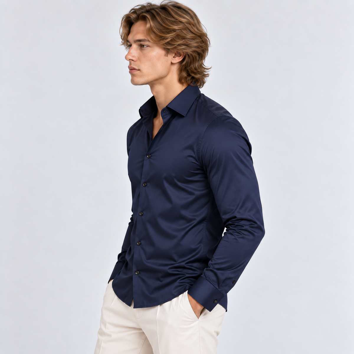 Side view of a man wearing a navy blue long sleeve button-down shirt with white trousers