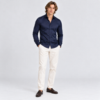 Man wearing a navy blue button-down shirt with white trousers and dark loafers