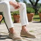 Person wearing beige loafers sitting outdoors with white pants and potted plants in the background.