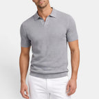Man wearing a gray patterned polo shirt and white pants on a light gray background