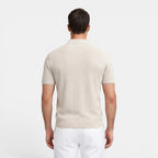 Man wearing a beige polo shirt and white pants on a light gray background
