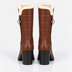 A pair of mid-calf brown boots with a cream shearling lining at the collar and black block heels, shown from the back on a light gray background.