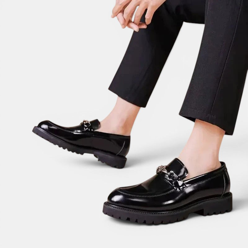 Black shiny loafers worn with black pants on a light gray background