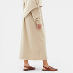 Person wearing a long beige coat and brown sandals on a white background