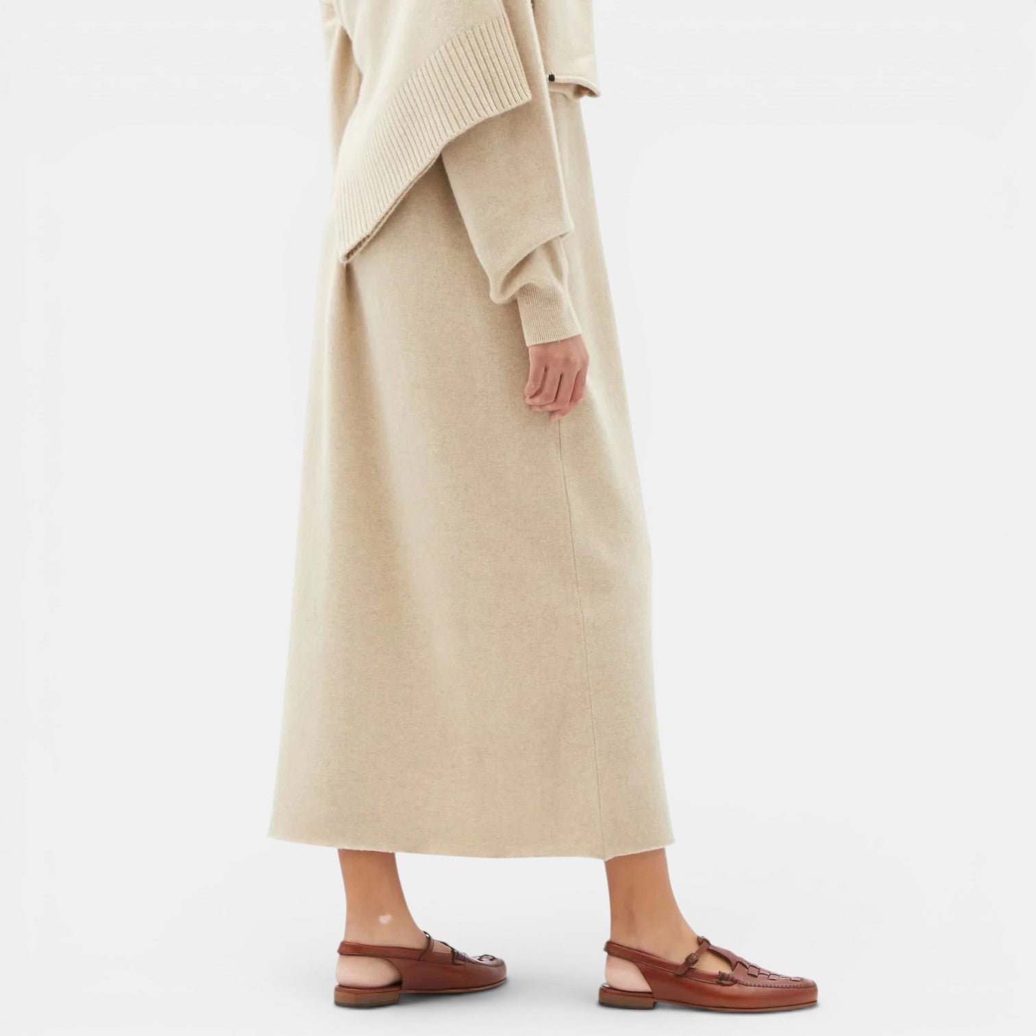 Person wearing a long beige coat and brown sandals on a white background