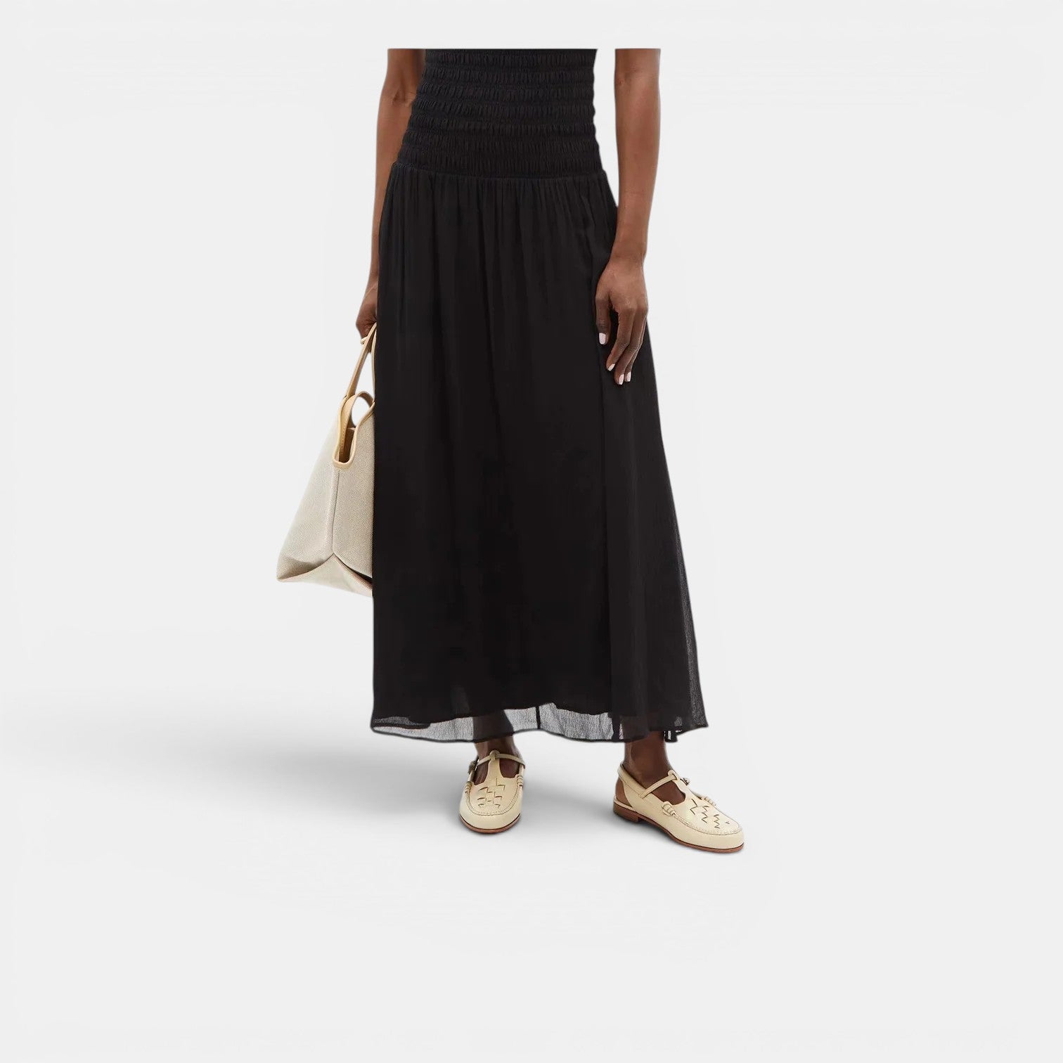 Person wearing a black dress holding a beige handbag on a white background