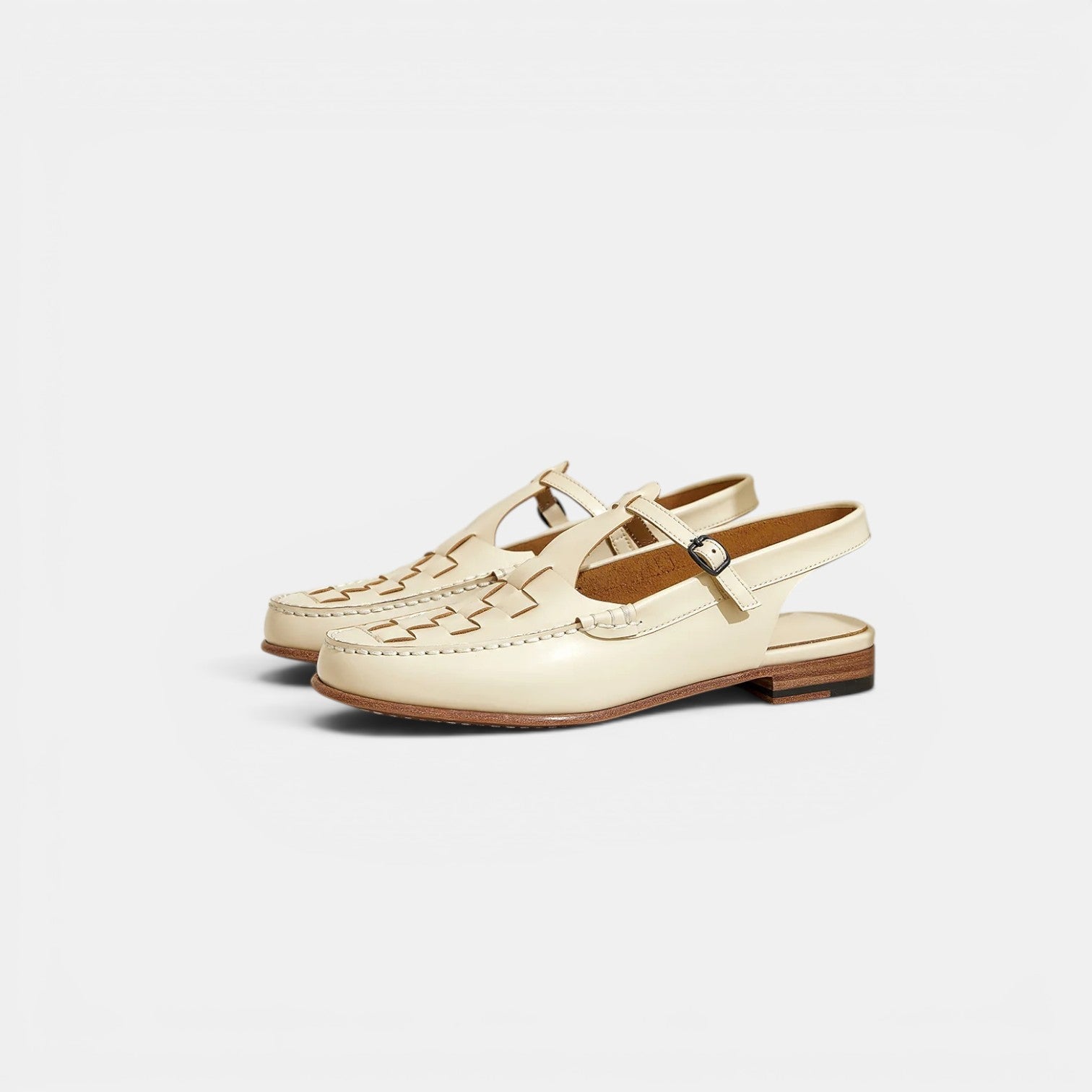 Pair of cream-colored loafers with a strap on a light gray background