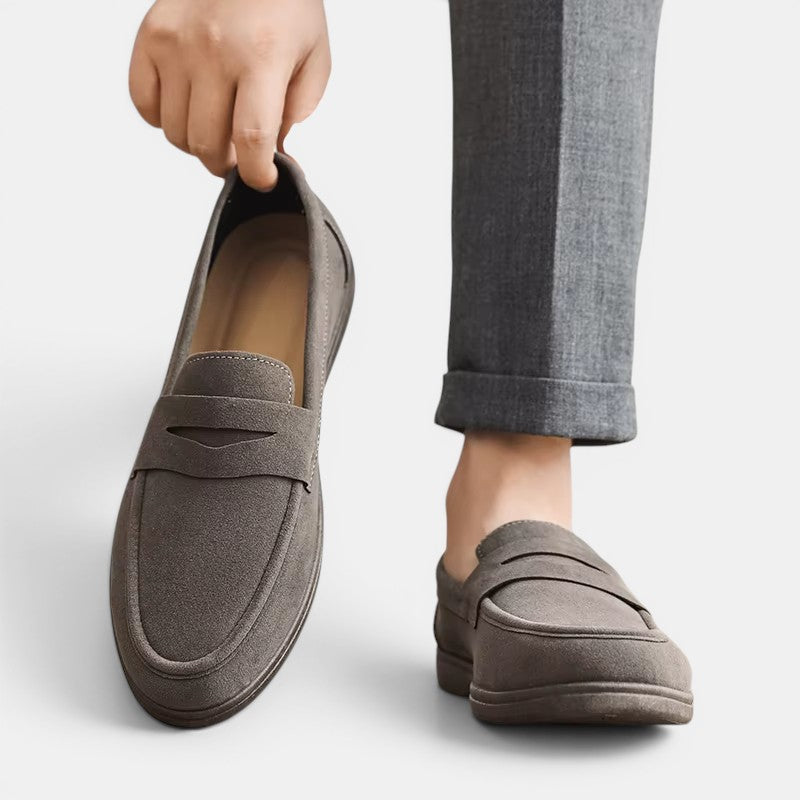 Gray loafers being held up with a person wearing gray pants on a white background