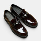 Pair of brown loafers with metallic buckles on a light gray background