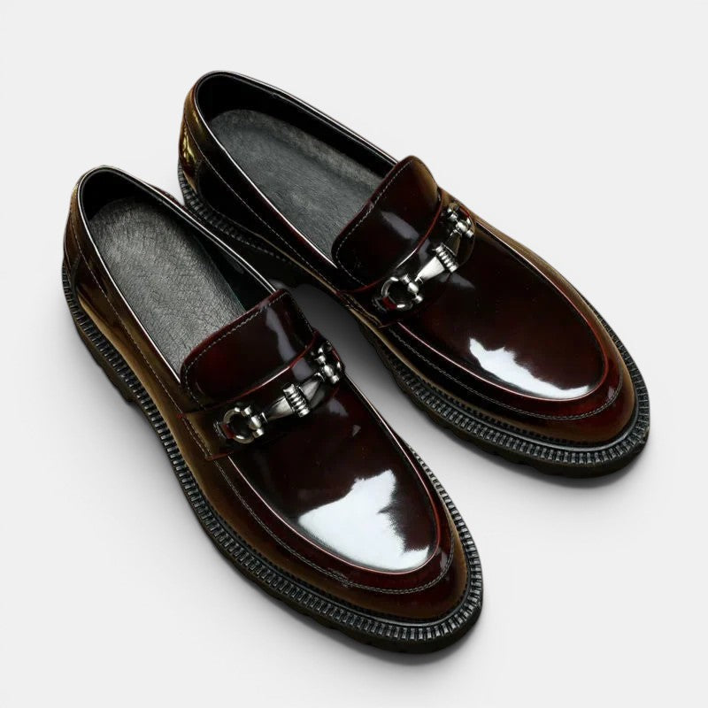 Pair of brown loafers with metallic buckles on a light gray background