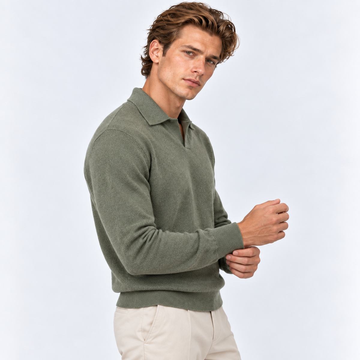 A man wearing a muted sage green knit polo sweater and light beige trousers, posed against a clean light gray studio background.