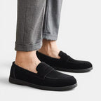 Black loafers worn with gray pants on a light background