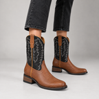 Woman wearing tan leather cowboy boots with black embroidered shafts and black jeans
