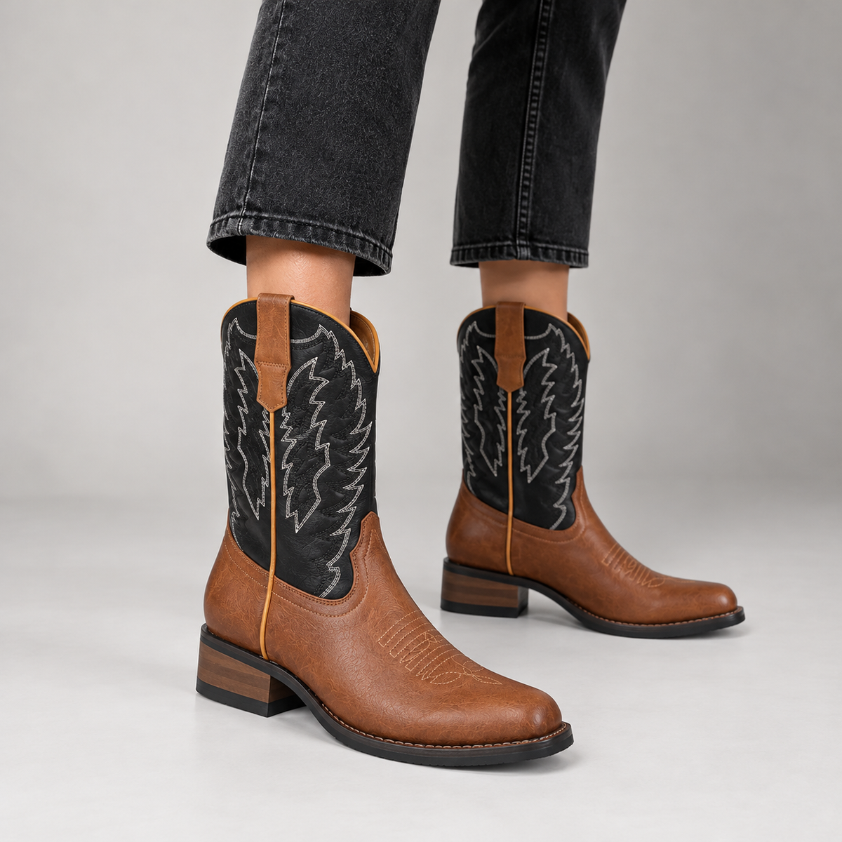 Woman wearing tan leather cowboy boots with black embroidered shafts and black jeans