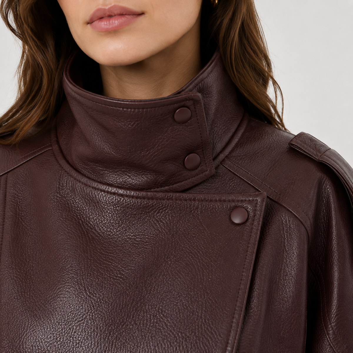 Close-up of a model wearing a dark brown textured leather jacket with a high buttoned collar and asymmetrical snap detail.