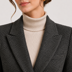 Close-up of a person wearing a dark gray and black herringbone blazer over a cream ribbed turtleneck sweater.