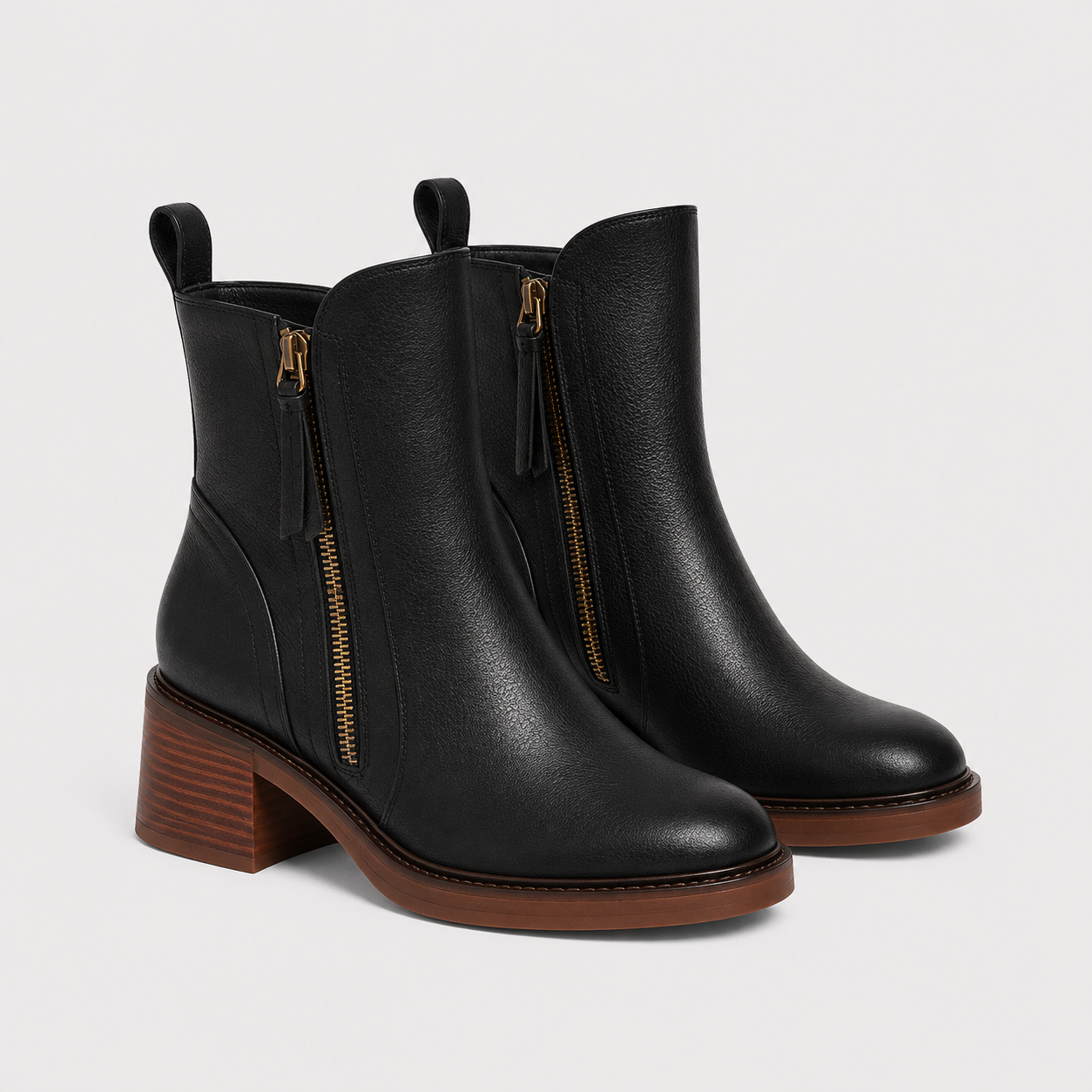 A pair of black leather ankle boots with side zippers, a low stacked block heel, and a brown sole, shown on a light gray background.