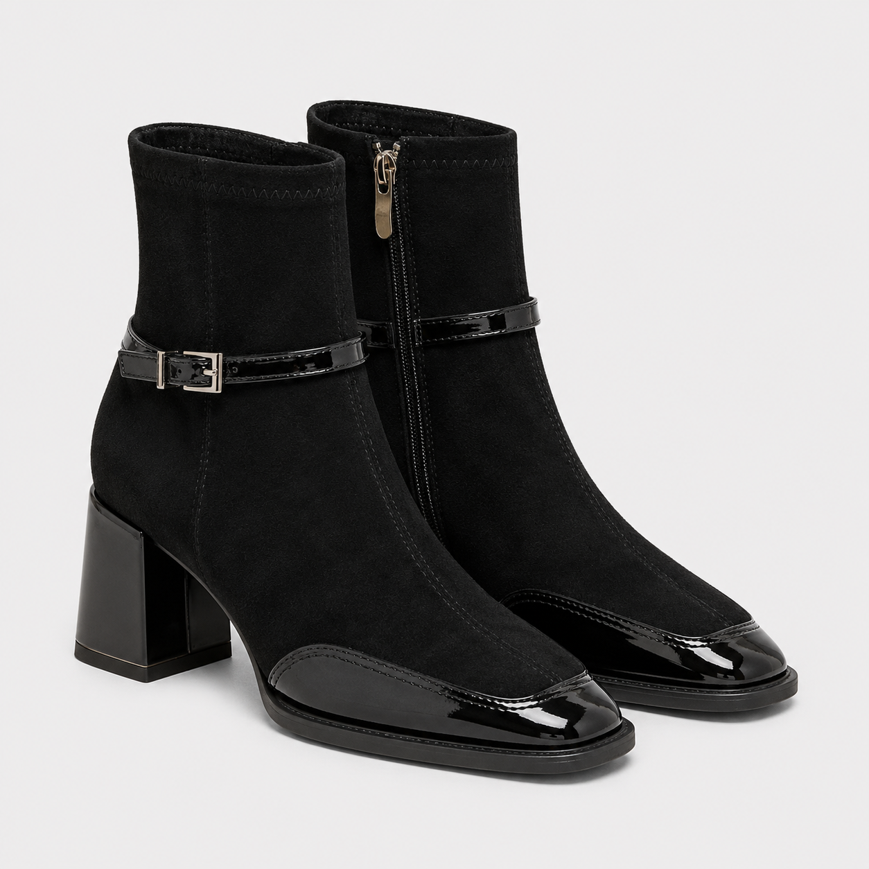 A pair of black ankle boots with a mix of matte suede and glossy patent leather, featuring a block heel, pointed toe, and side zipper.