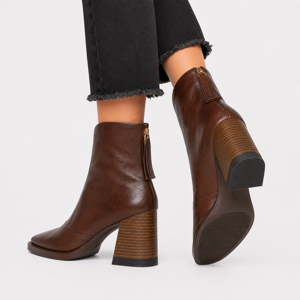 A pair of dark brown leather ankle boots with block heels, shown on a model wearing black frayed-hem jeans against a light gray background.