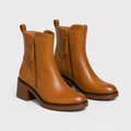 A pair of tan leather ankle boots with side zippers, pull tabs, and low block heels, shown on a light gray background.