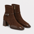 A pair of brown suede ankle boots with patent leather toe caps, block heels, and side buckle straps, shown on a light gray background.