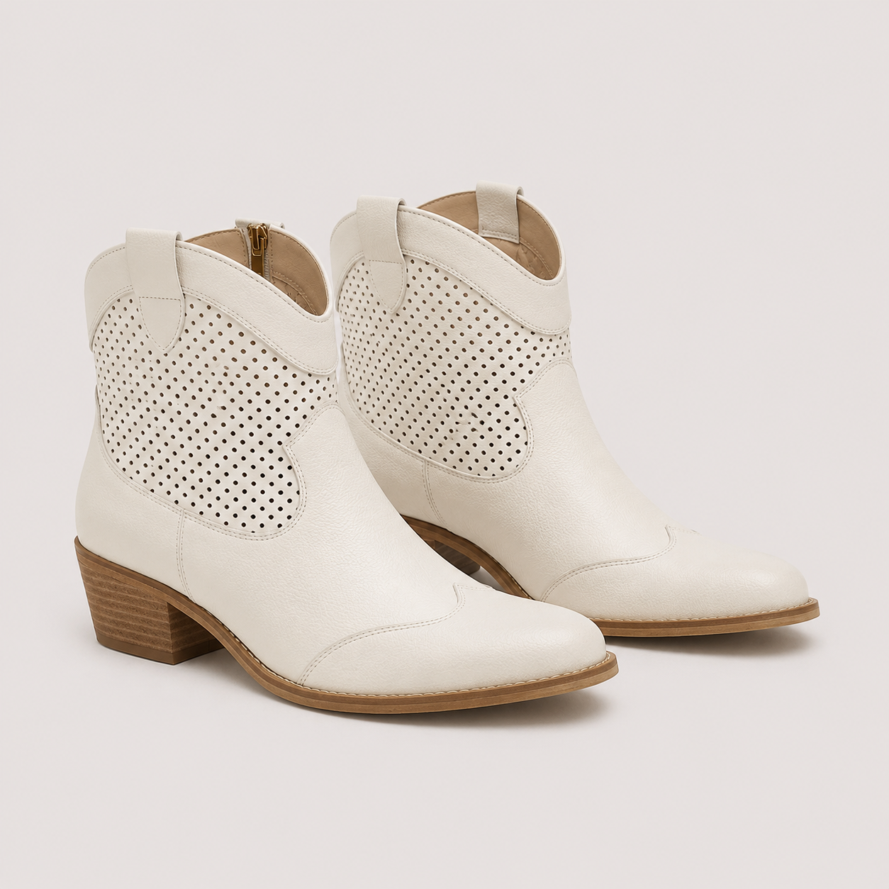 A pair of off-white leather western ankle boots with perforated side panels and low stacked wood-look heels, shown on a light beige background.